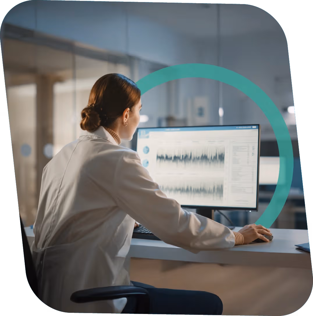 Woman in a white lab coat analyzing data charts on a computer monitor